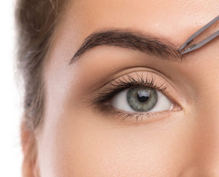 Close up of female face and eyebrow with tweezers
